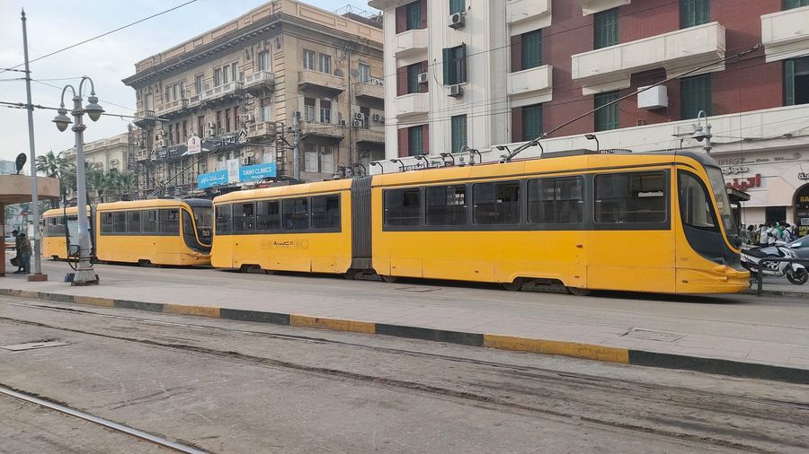 Two yellow trams on the tracks in downtown Alexandria, Egypt, backed by early-20th-century apartment buildings