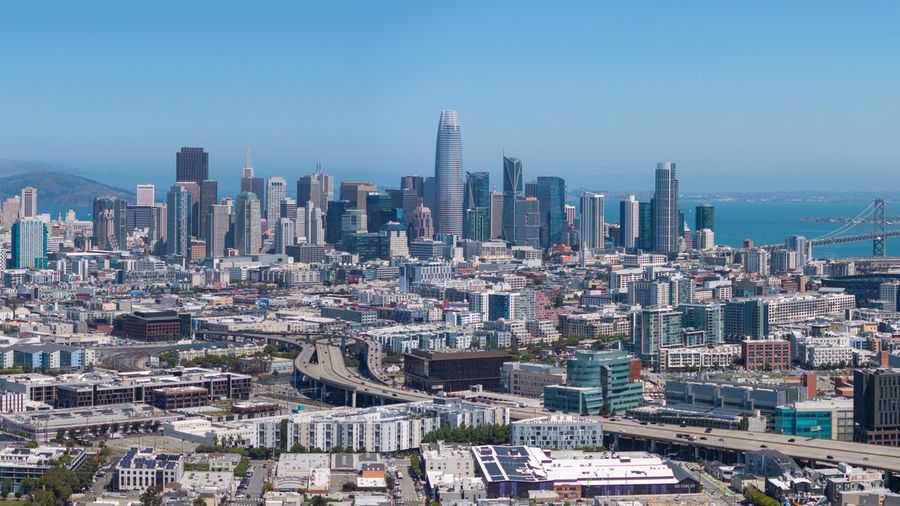 The San Francisco skyline under a clear blue sky, with the rounded Salesforce Tower rising above downtown high-rises and the Bay Bridge to the right