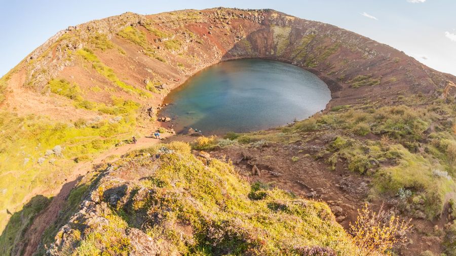 The turquoise crater lake of Kerið ringed by red and black volcanic scree near Selfoss in South Iceland, seen from the rim path on a bright summer day